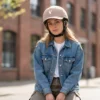 Vrouw met spijkerjas draagt beige fietshelm met pet en hertenlogo